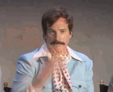 Gif of man with a mustache in blue suit with pink neckerchief throwing up glitter