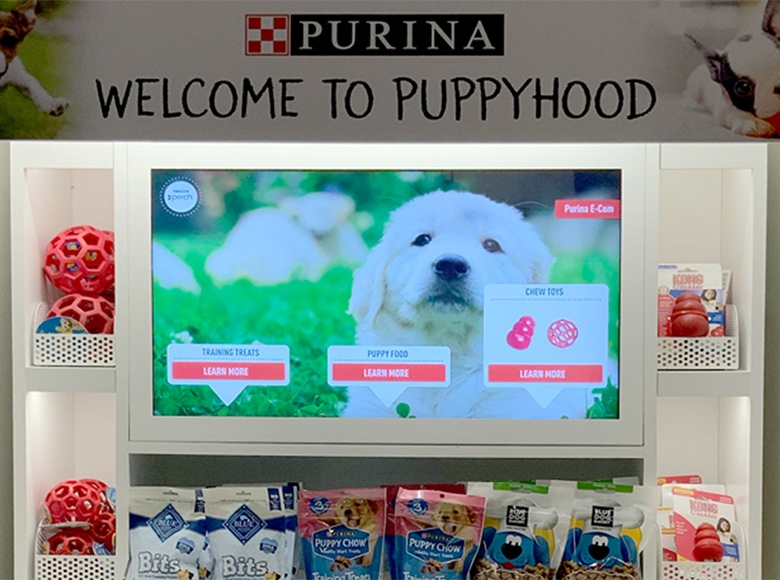 picture of a screen surrounded by purina items. The screen is touchscreen with a puppy and different buttons to "learn more"