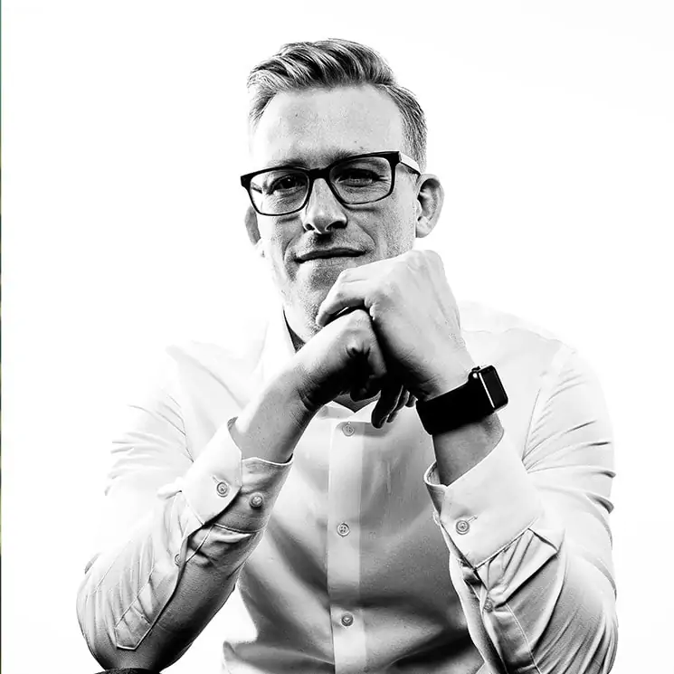 a black and white photo of greg, a man with light hair and glasses who is looking pensive