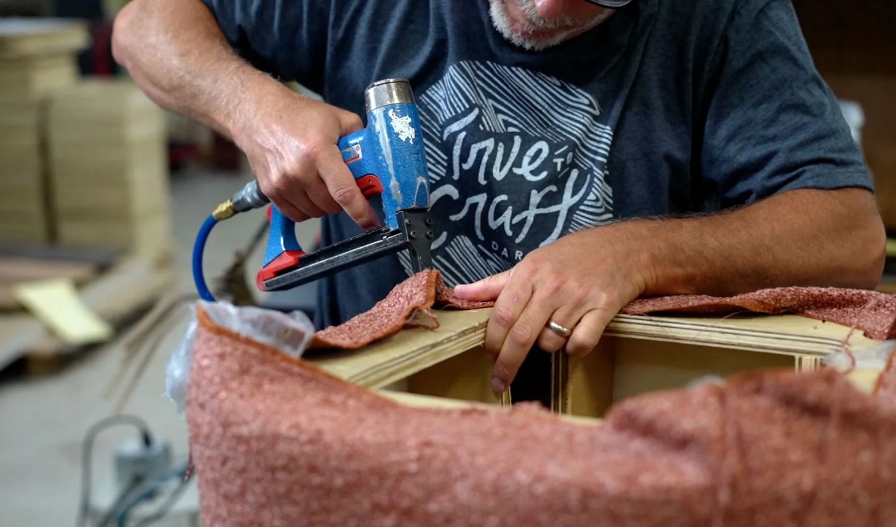 a close up image of worker stapling fabric to a piece of furniture in a workshop